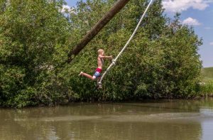 boy on rope swing over lake