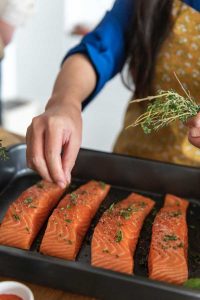 woman adding herbs to salmon
